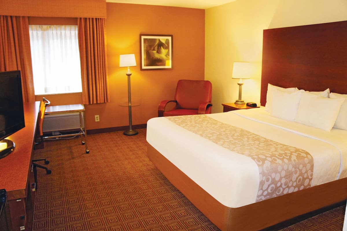 A hotel room with a large bed, a desk with a computer, a chair, and a lamp.