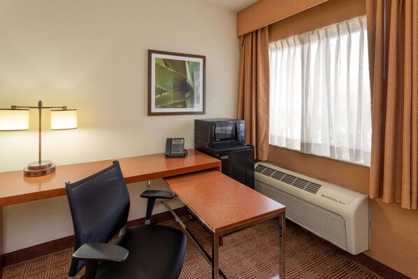 Habitación de hotel con escritorio, silla, microondas, teléfono, aire acondicionado y ventana con cortinas.