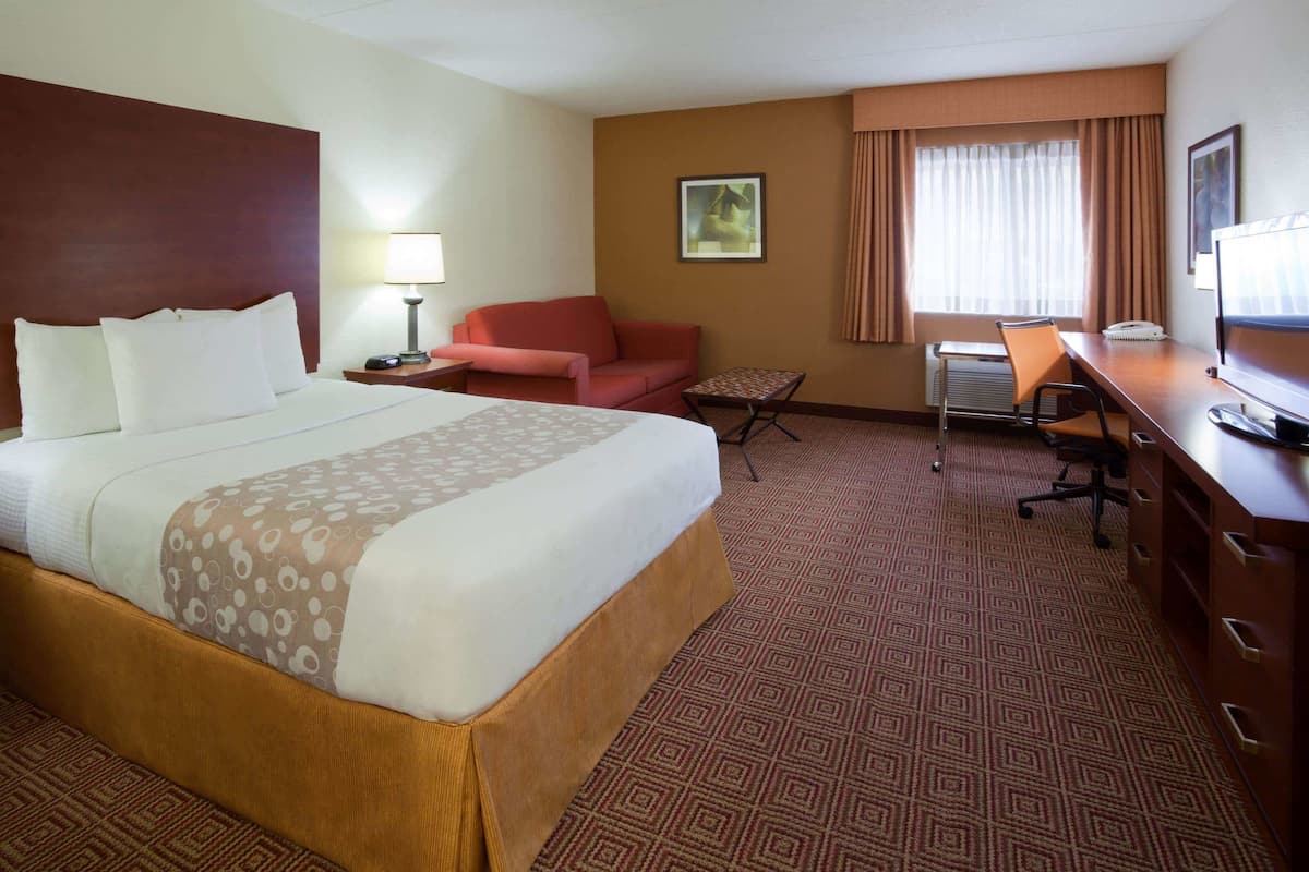 A hotel room with a large bed, a desk with a computer, a chair, a small table, and a couch.