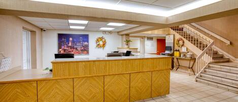 A reception area with a wooden counter, a cityscape poster, a wreath, and a staircase.