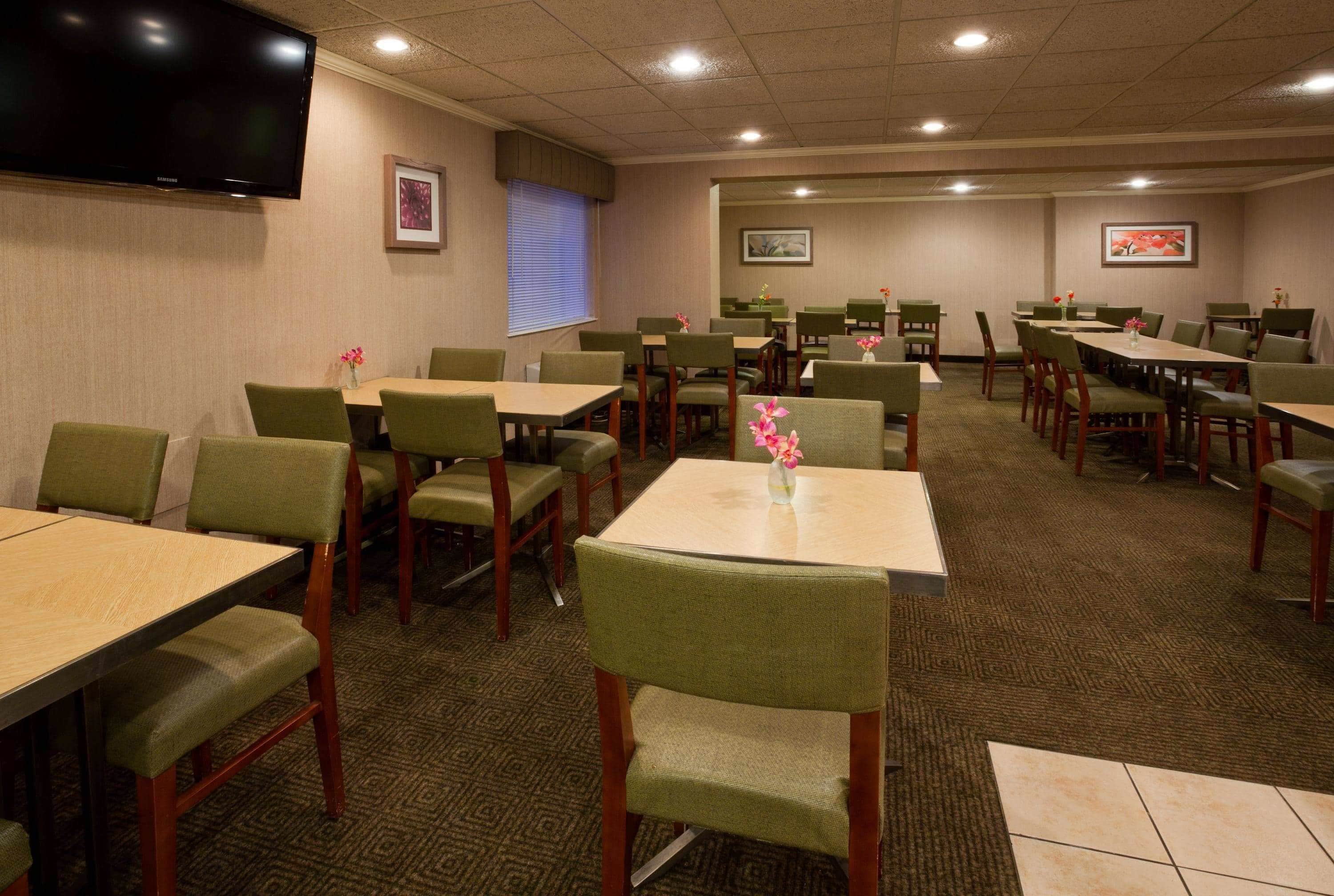 A conference room with multiple tables and chairs, a flat-screen TV mounted on the wall, and framed artwork on the walls.