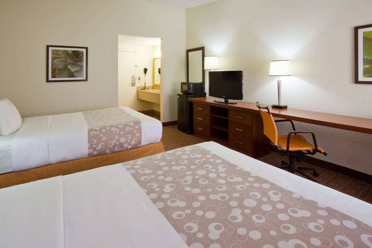 A hotel room with two beds, a desk with a chair, a television, and a mirror.