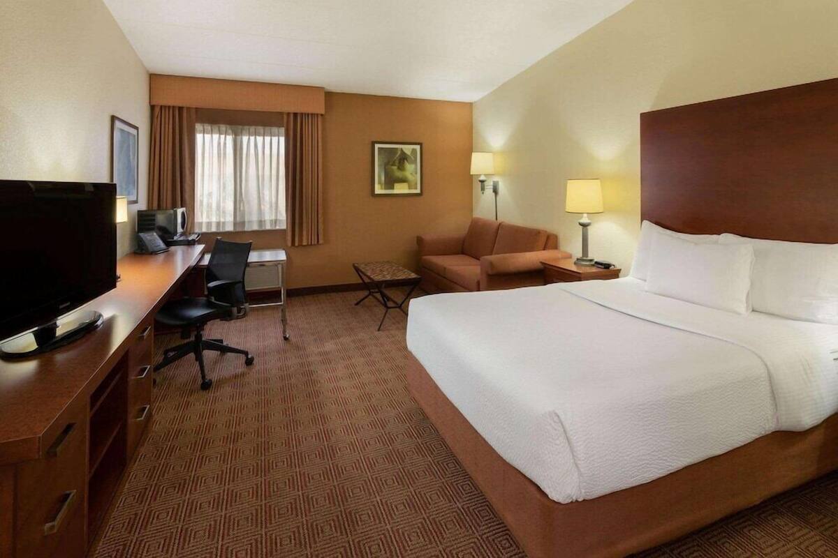 Una habitación de hotel con una cama grande, un escritorio con computadora, una silla y un televisor.