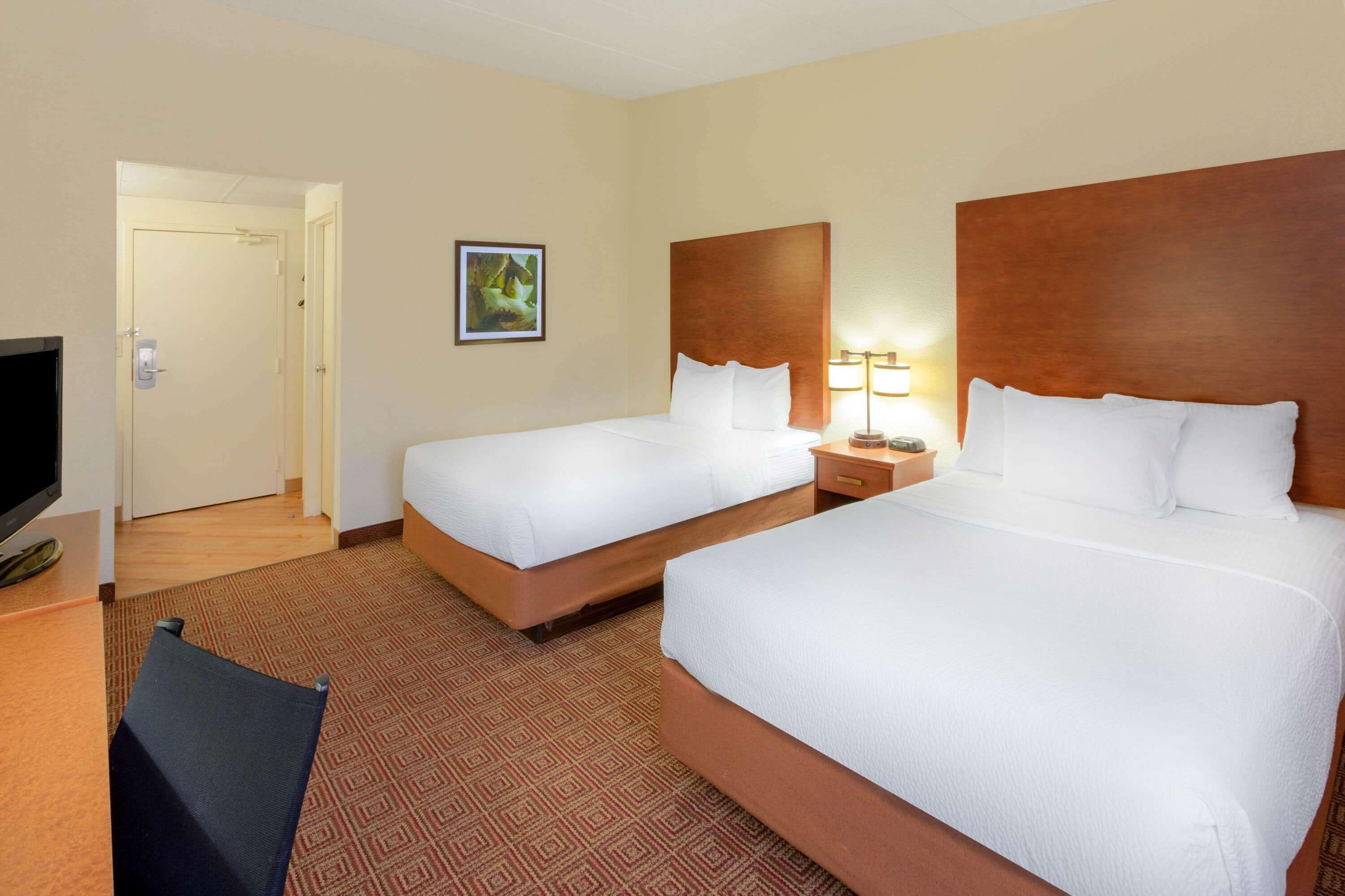 A hotel room with two beds, a TV, a desk, and a door leading to another room.