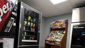 Una máquina expendedora, una exhibición de bocadillos y un dispensador de bebidas en una habitación limpia con baldosas.