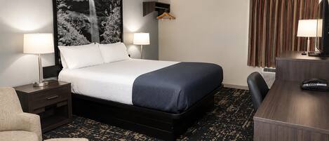 Habitación de hotel con una cama, dos lámparas de noche, un escritorio con teléfono, una silla y un cuadro abstracto grande en la pared.