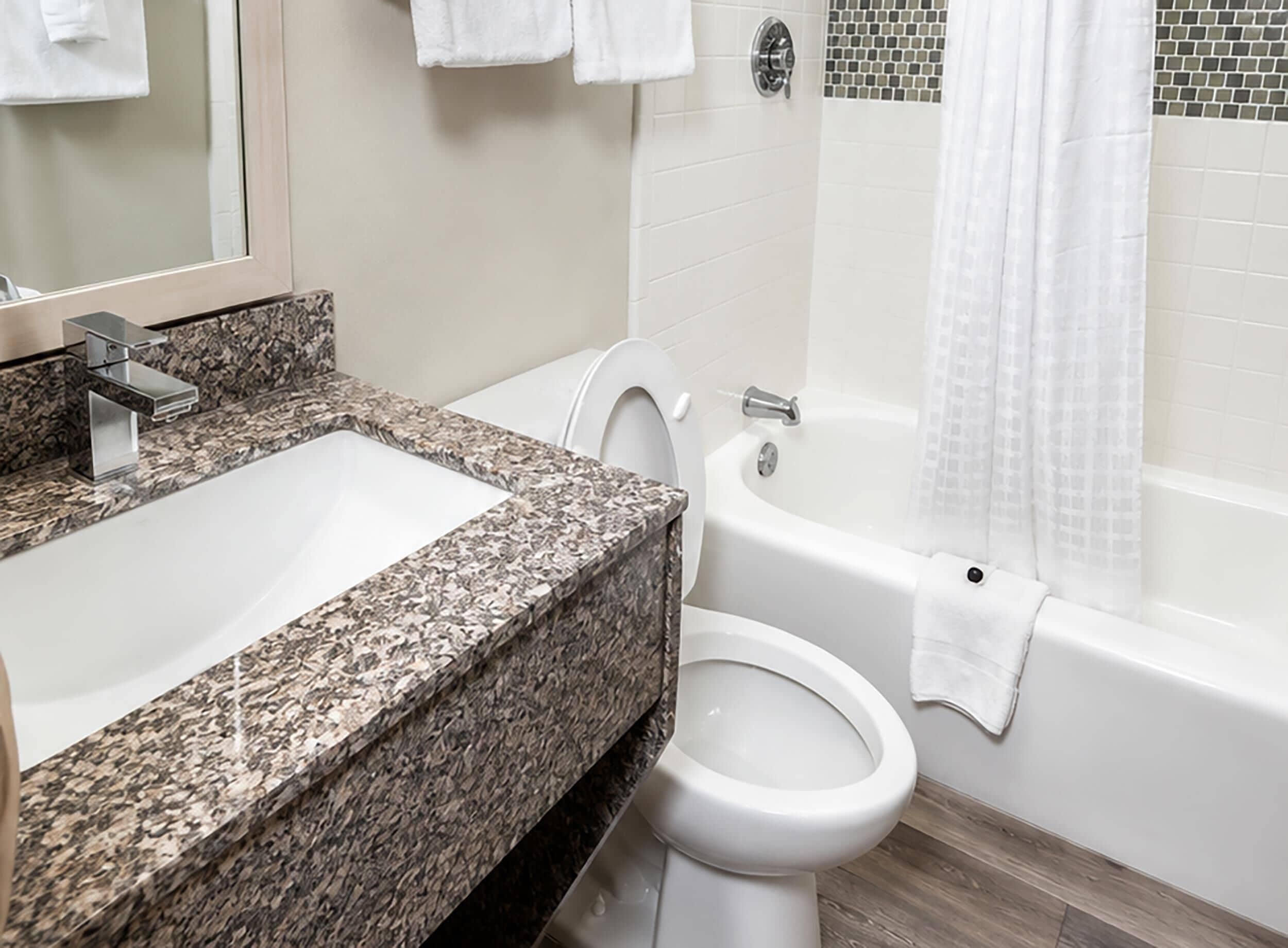 A bathroom with a granite countertop sink, a toilet, and a bathtub.