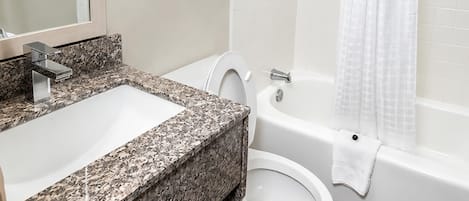 A bathroom with a granite countertop sink, a toilet, and a bathtub.