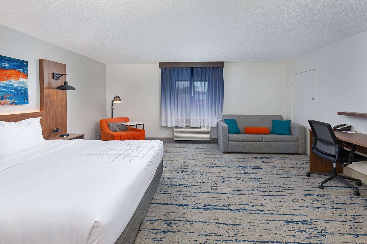 A hotel room with a bed, a desk, a chair, a sofa, and a window with curtains.