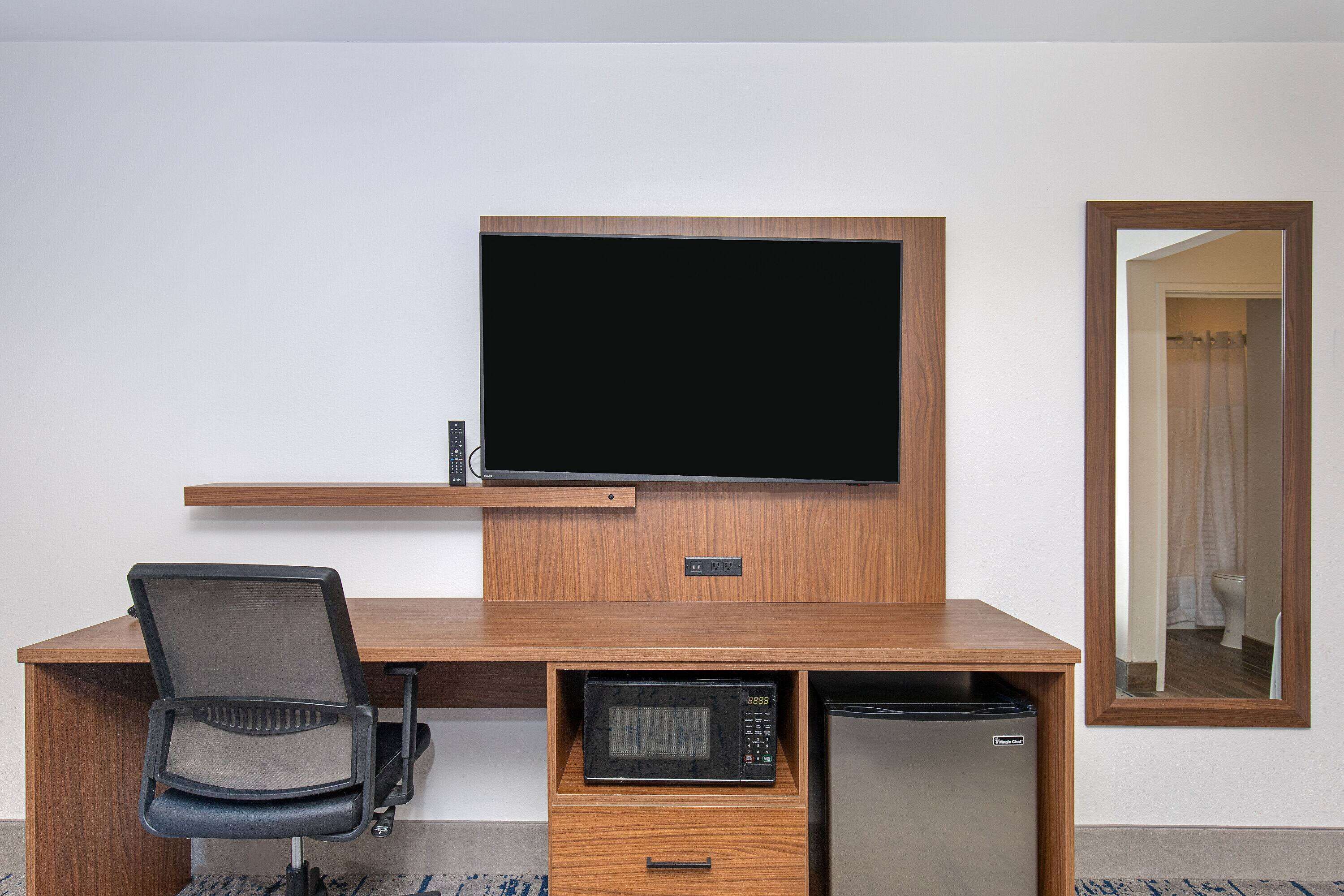 Habitación de hotel con escritorio de madera, televisor, microondas y refrigerador.