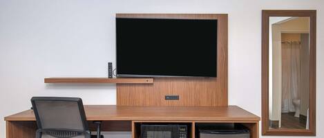 Habitación de hotel con escritorio de madera, televisor, microondas y refrigerador.