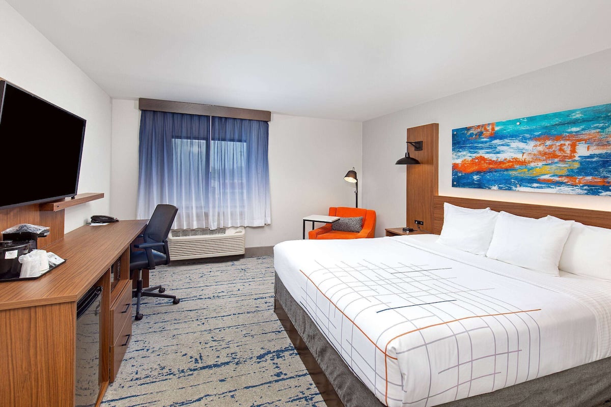 A hotel room with a large bed, a desk with a computer, a chair, a TV, and a painting on the wall.