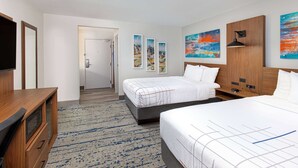 Habitación de hotel con dos camas, un televisor, un aparador de madera y un pasillo que conduce a un baño.