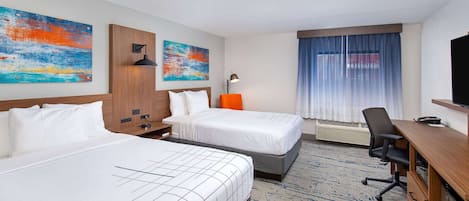 A hotel room with two beds, a desk, a chair, a TV, and artwork on the walls.