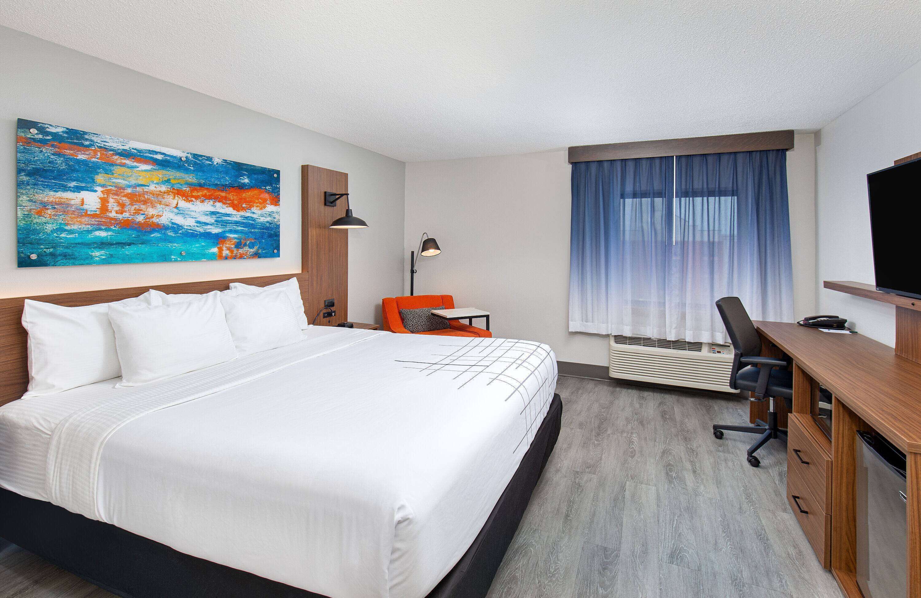 Une chambre d’hôtel avec un grand lit, un bureau, une chaise, une télévision et un tableau au mur.