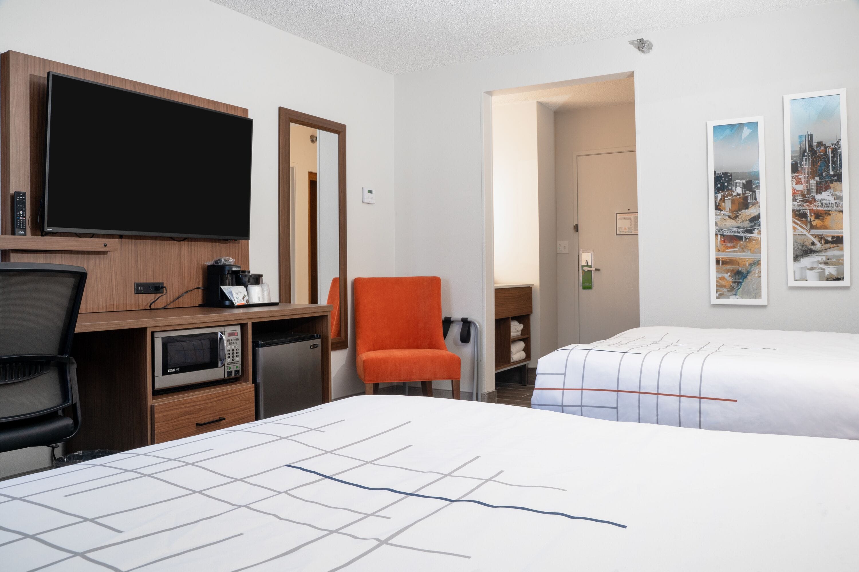 A hotel room with a TV, microwave, coffee maker, and a desk. There are two beds with white bedding and a chair.