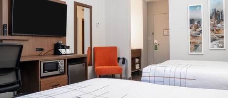 A hotel room with a TV, microwave, coffee maker, and a desk. There are two beds with white bedding and a chair.