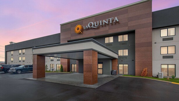 Un hotel moderno con un llamativo letrero de 'La Quinta', estacionamiento cubierto y un exterior bien cuidado.