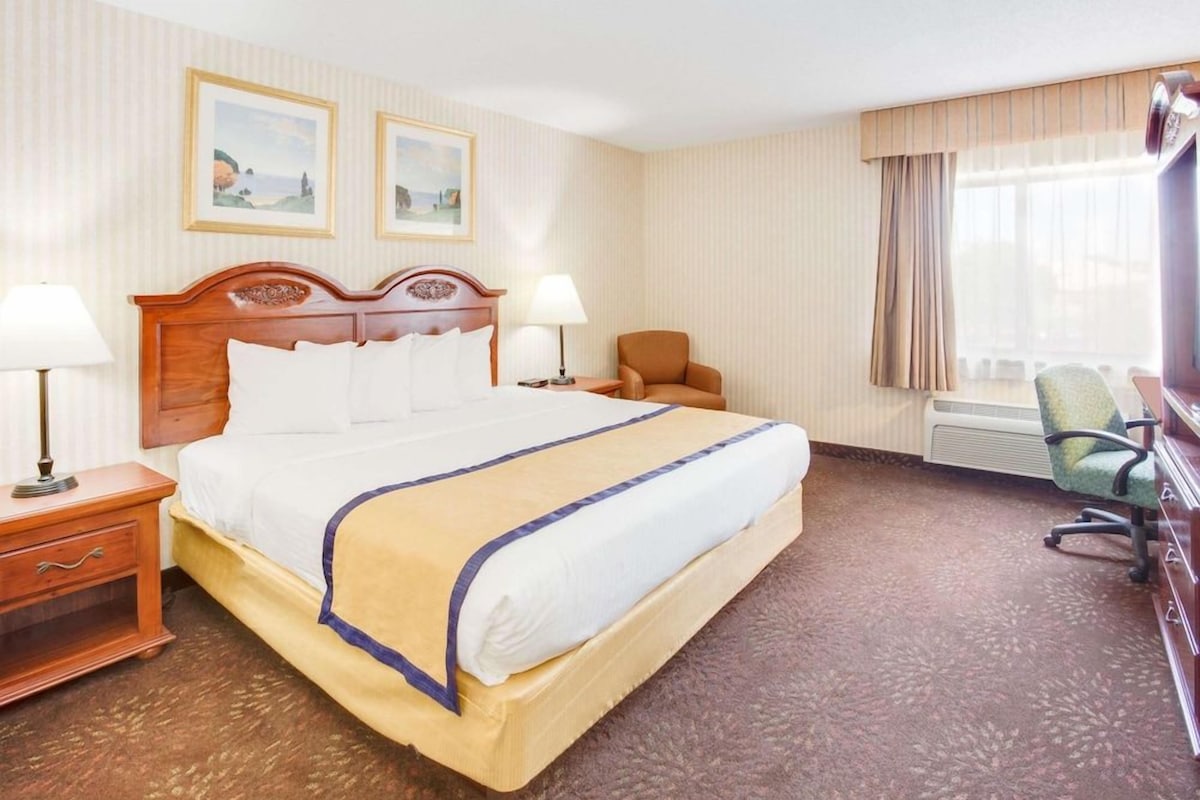 A hotel room with a large bed, two bedside tables, a chair, a desk, and a window with curtains.