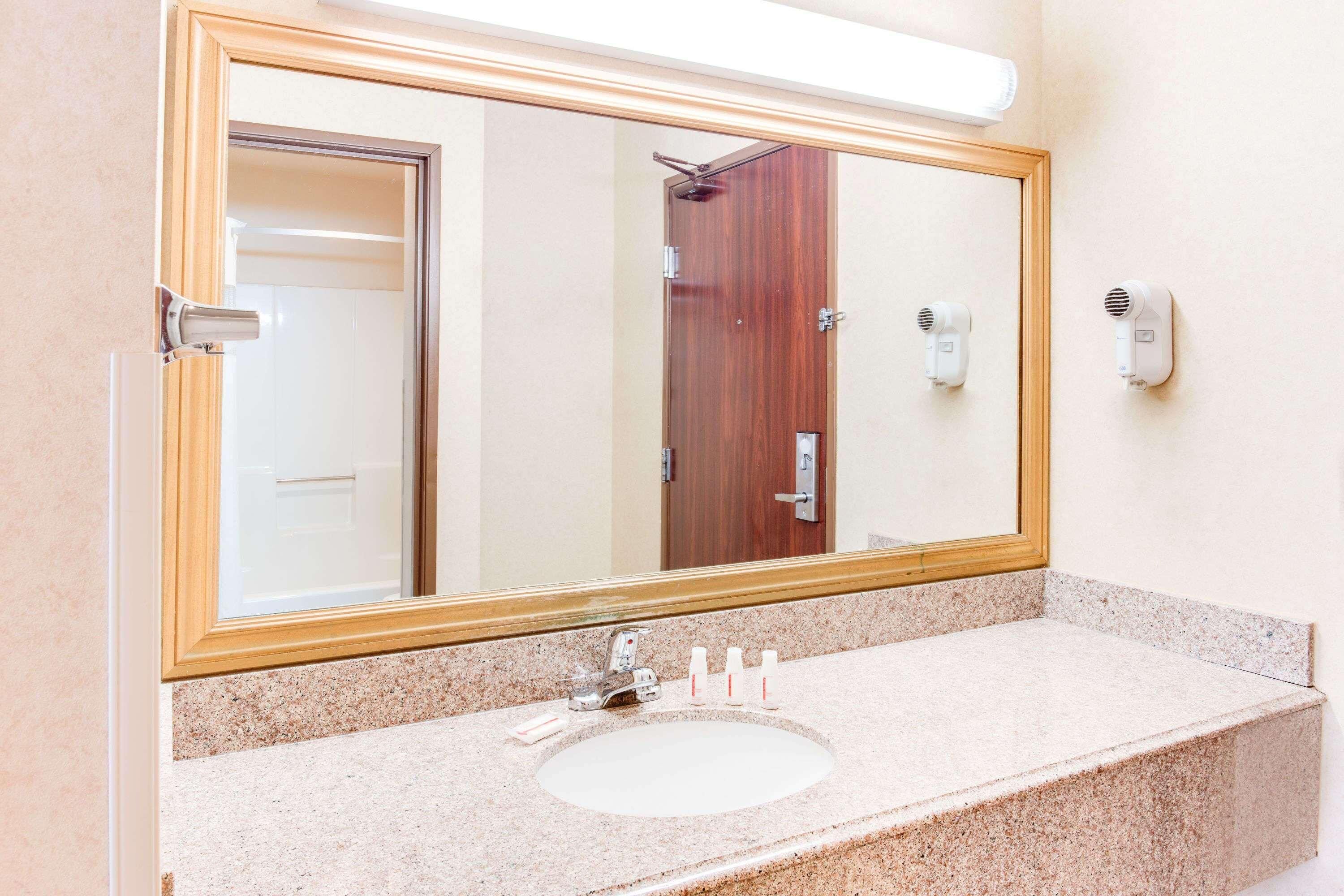 Un baño con un espejo grande, un lavamanos y dos secadores de pelo sujetos a la pared.