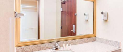 Un baño con un espejo grande, un lavamanos y dos secadores de pelo sujetos a la pared.