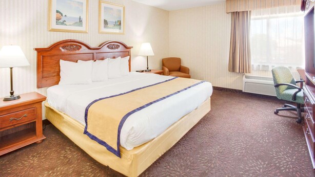 A hotel room with a large bed, two bedside tables, a chair, a desk, and a window with curtains.