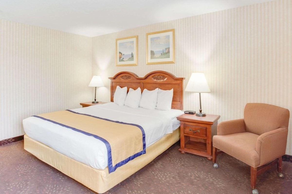 A hotel room with a bed, two bedside tables, a chair, and two framed pictures on the wall.
