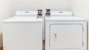 Two white front-loading washing machines in a laundry room with a door on the right side.