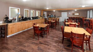 Un grand espace à manger avec des tables et des chaises en bois, un comptoir de cuisine équipé d’appareils électroménagers et un grand miroir au mur.