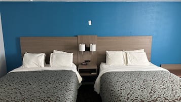 A hotel room with two beds, a nightstand with a lamp, and a wall clock.