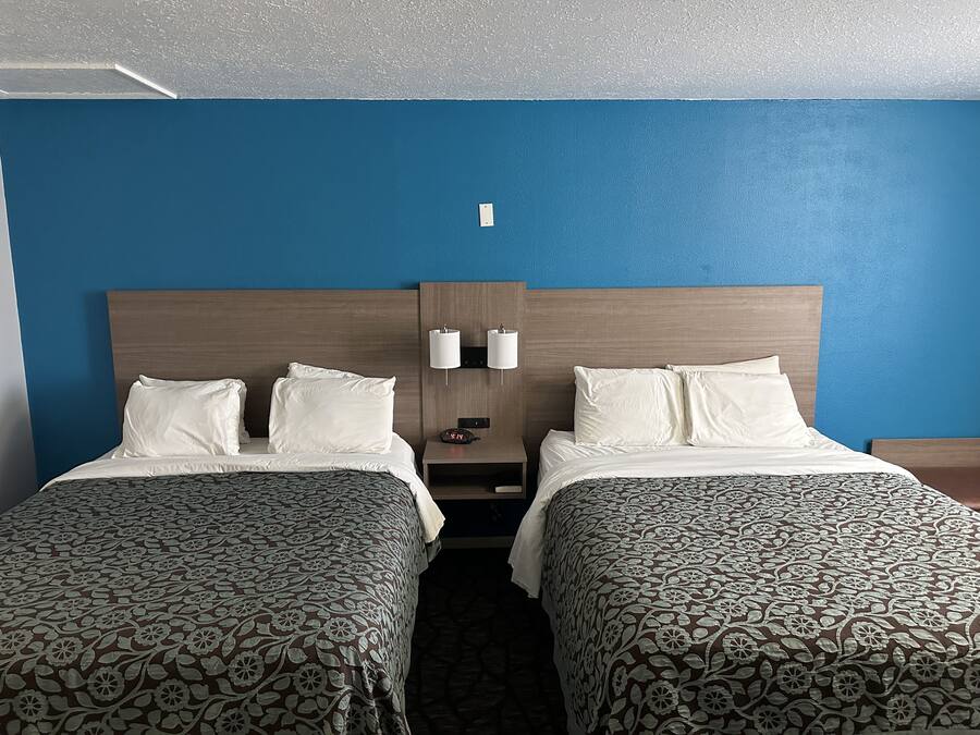 Ein Hotelzimmer mit zwei Betten, einem Nachttisch mit Lampe und einer Wanduhr.