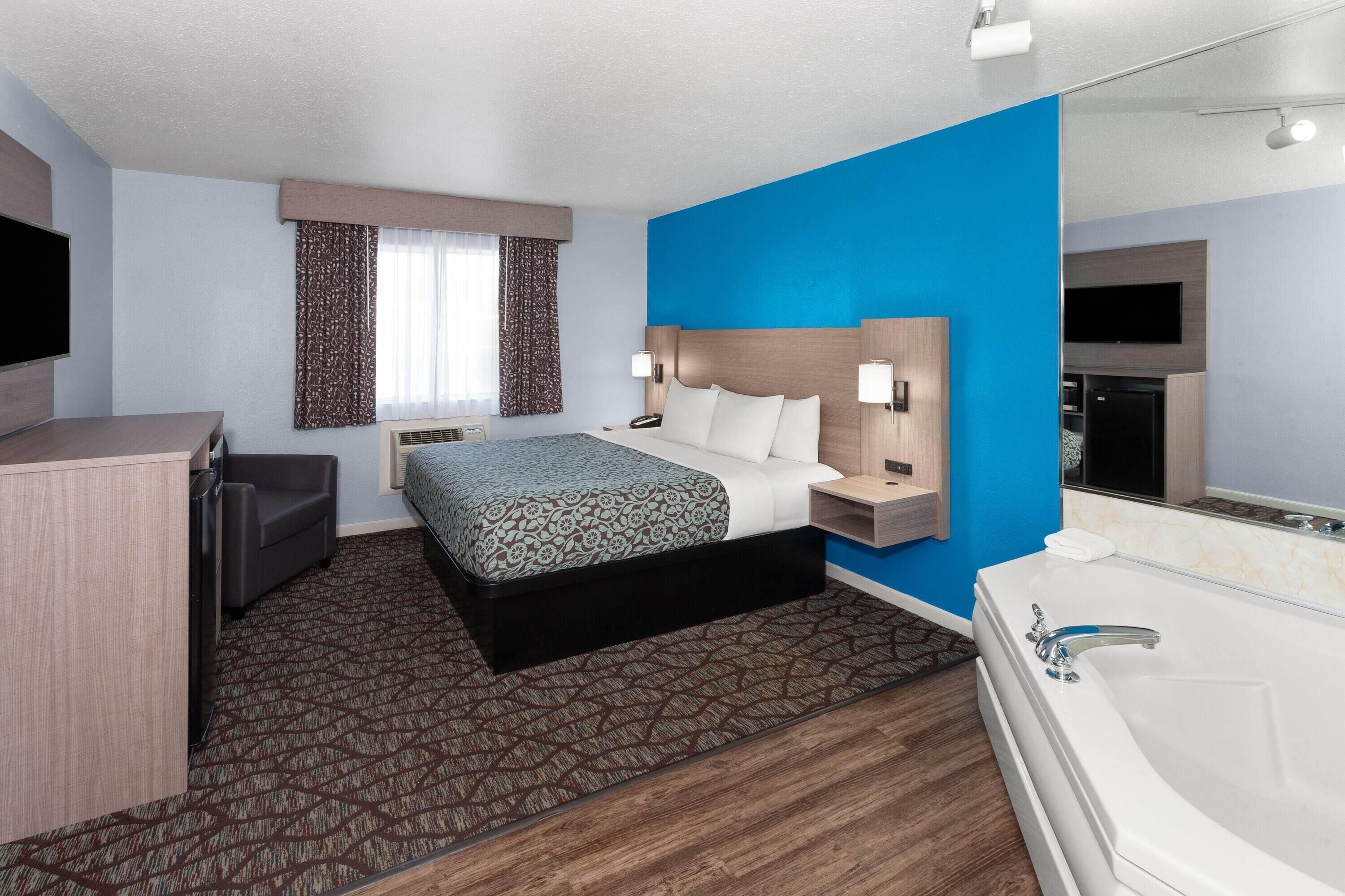 A hotel room with a bed, bedside tables, a desk, a TV, a bathroom with a bathtub, and a window with curtains.