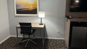 Une chambre d’hôtel équipée d’un bureau, d’une chaise, d’une lampe, d’une télévision et ornée d’un tableau représentant un coucher de soleil.