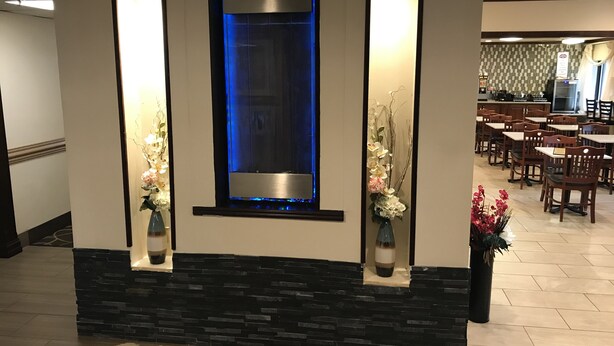 A reception area with a stone accent wall, a blue-lit water feature, and two vases with flowers.