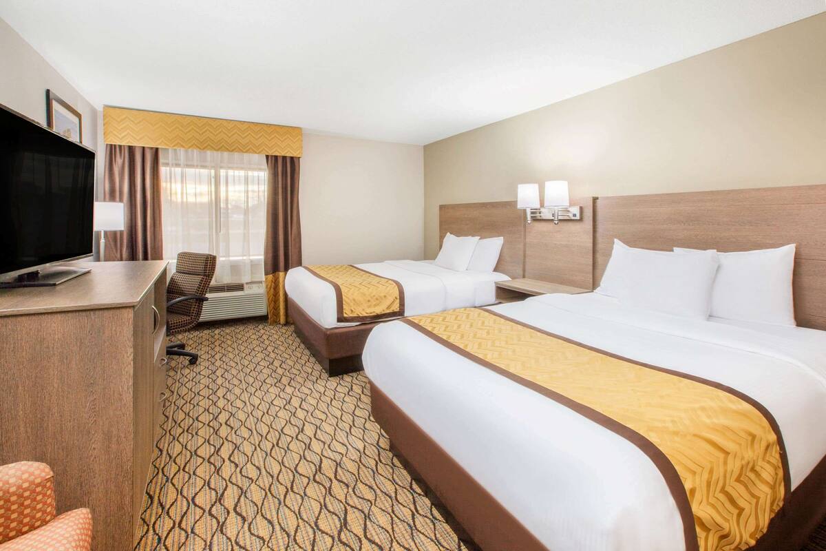 A hotel room with two beds, a desk with a television, and a chair.
