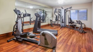 A gym with various exercise equipment, wooden flooring, and a large mirror on the wall.
