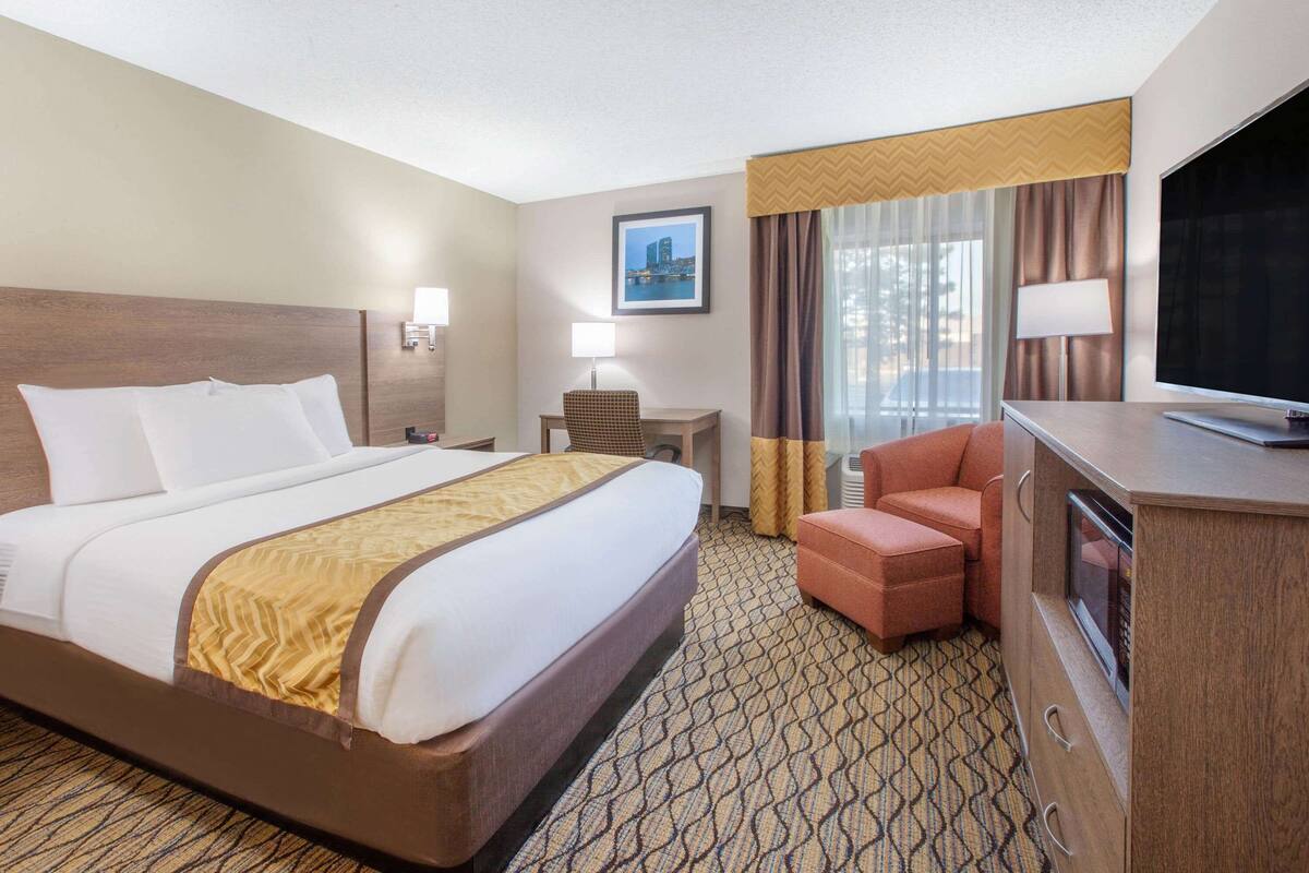 A hotel room with a large bed, a desk, a chair, a television, and a minibar.