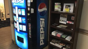 Pepsi-logolla varustettu myyntiautomaatti ja hylly, jossa on lehtiä ja esitteitä.