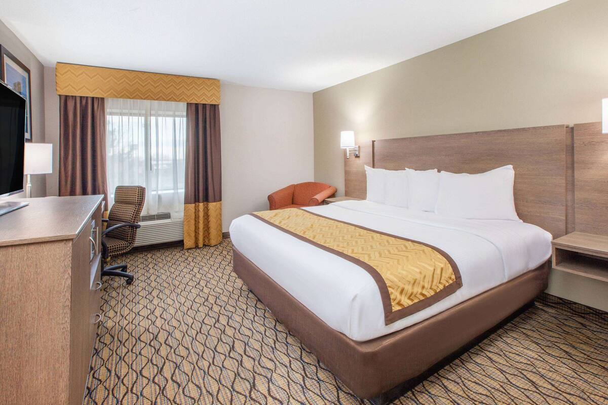 A hotel room with a large bed, a desk, a chair, and a television.