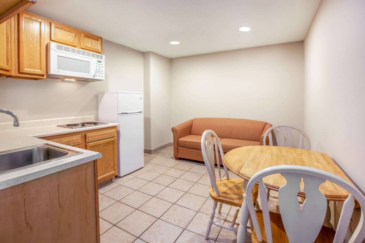 A compact kitchen with wooden cabinets, a microwave, a refrigerator, a sink, and a dining area with a table and chairs.