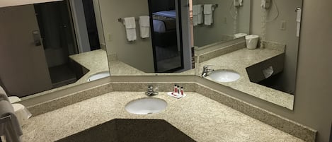 A bathroom with a granite countertop sink, a mirror, and a hairdryer on the wall.
