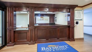 A reception desk with a 'Baymont Inn & Suites' sign, a blue mat at the entrance, and framed pictures on the wall.