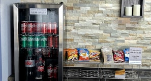 A vending machine stocked with sodas and snacks, a stone wall, and a sign offering snacks for $1.00.