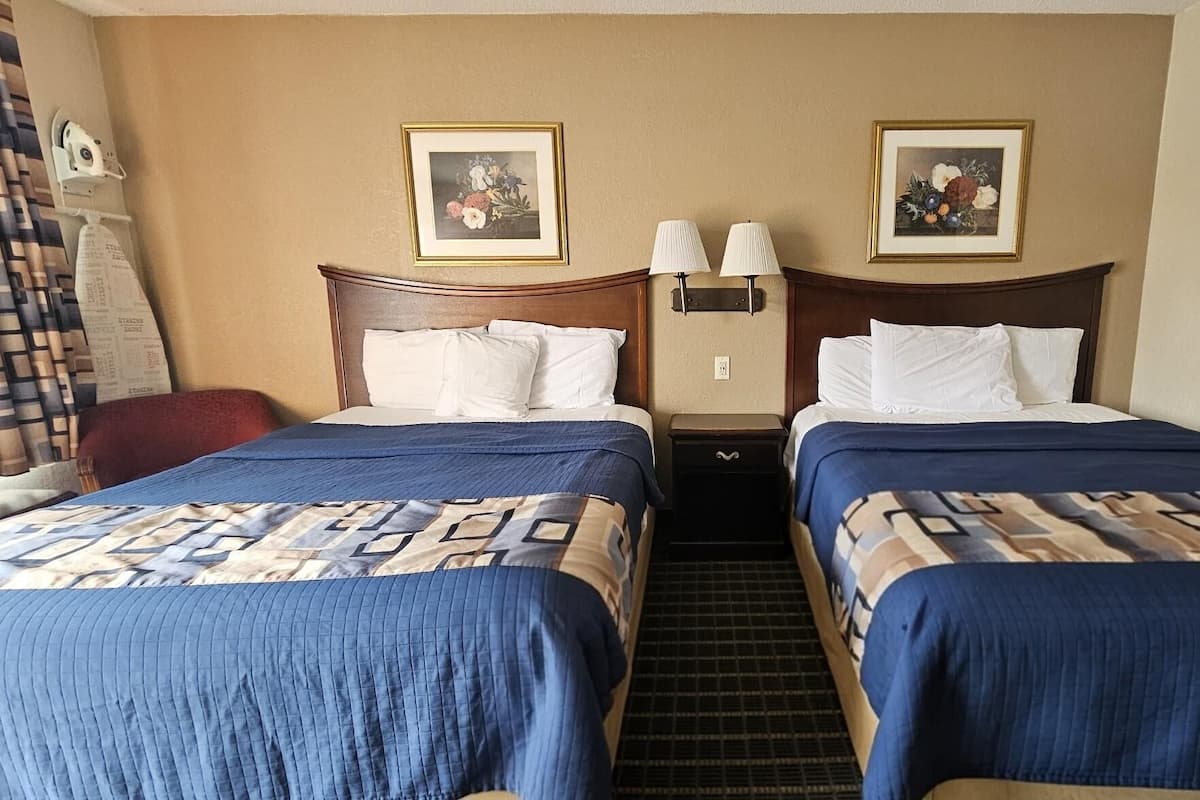 Une chambre d’hôtel avec deux lits, chacun recouvert d’une couvre-lit à motifs bleus et beiges, agrémenté d’oreillers blancs et doté d’une tête de lit en bois. Deux tableaux représentant des motifs floraux, encadrés, sont accrochés au mur au-dessus des lits.
