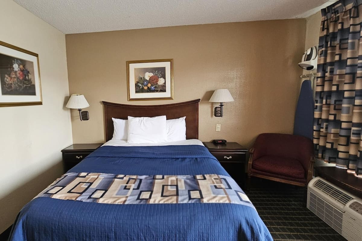 Une chambre d’hôtel comprenant un lit, deux tables de chevet, une chaise et deux lampes fixées au mur.
