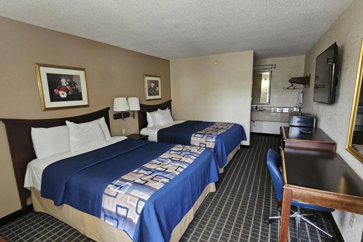 Une chambre d’hôtel avec deux lits, un bureau, une chaise, un miroir et deux lampes fixées au mur.