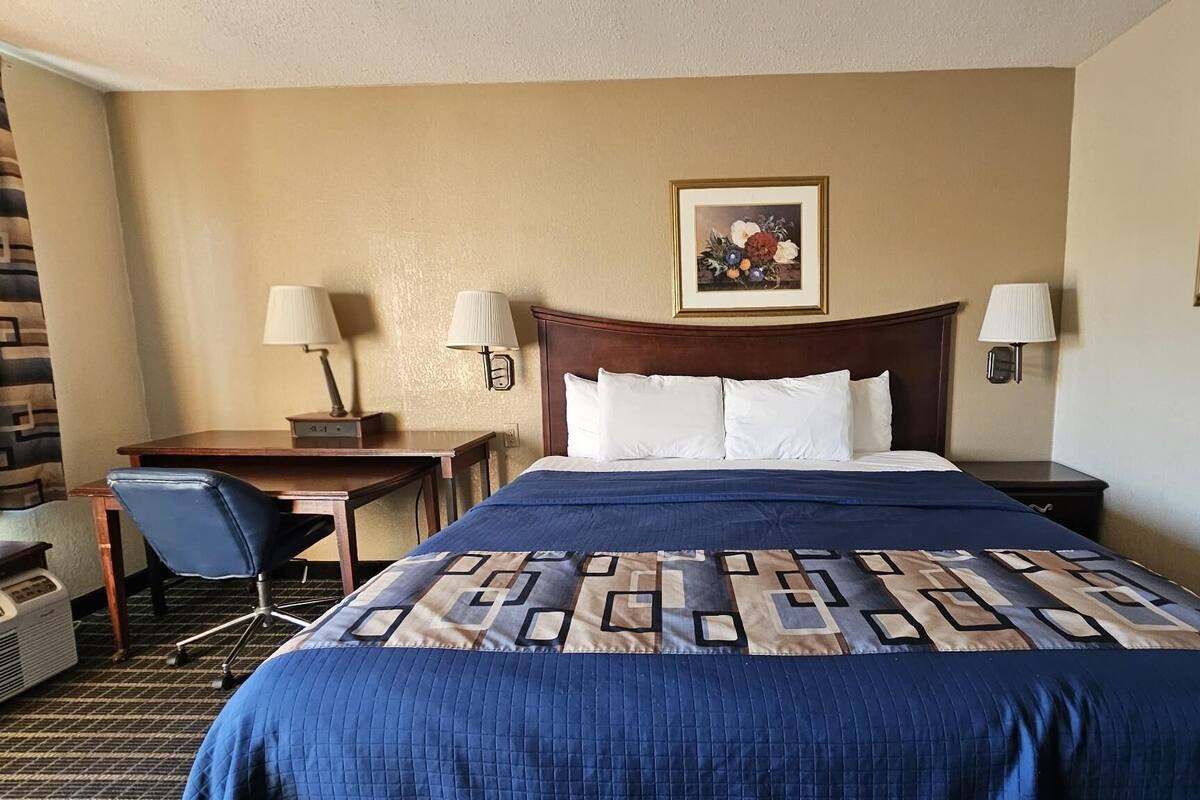 Une chambre d’hôtel avec un grand lit, deux tables de chevet avec des lampes, un bureau avec une chaise et un tableau accroché au mur.