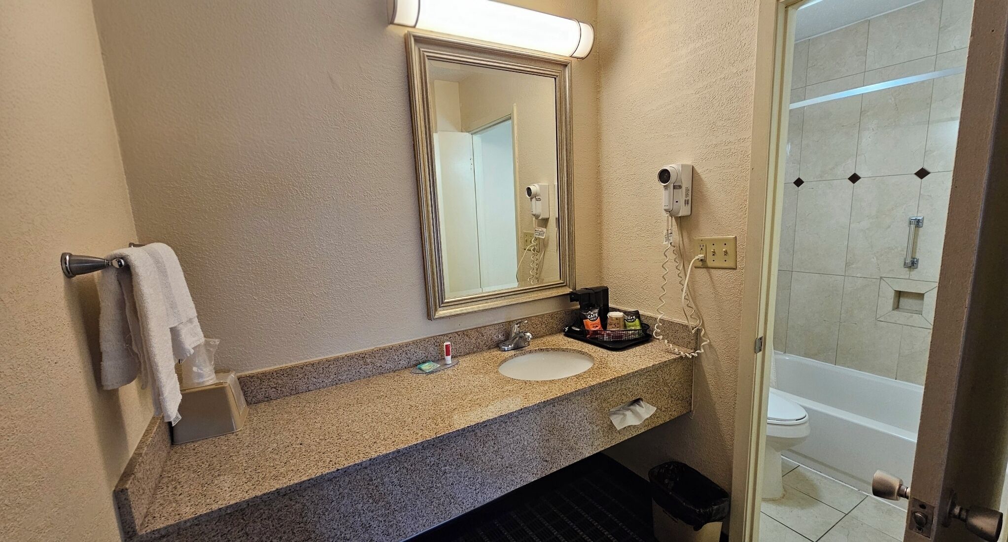 A bathroom with a granite countertop, a sink, a mirror, and a shower area.