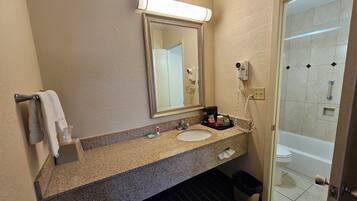 A bathroom with a granite countertop, a sink, a mirror, and a shower area.