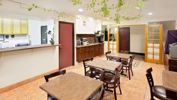 A dining area with tables and chairs, a kitchen area with a coffee machine, and a counter with a cash register. - Super 8 by Wyndham Yucca Val/Joshua Tree Nat Pk Area (Yucca Valley)